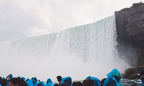 People by waterfall against sky