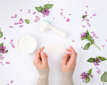 Directly above shot of hand around beauty product with flowers over white background