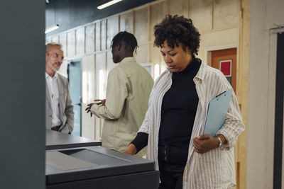 Businesswoman using photocopier machine with colleagues standing in background