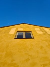 Low angle view of yellow building against clear blue sky