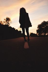 Silhouette woman standing on road against sky during sunset