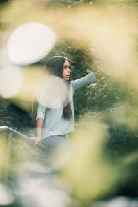 Girl sitting on railing of staircase against plants