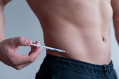 Midsection of shirtless man holding syringe