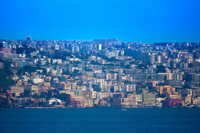 Aerial view of townscape by sea against clear blue sky