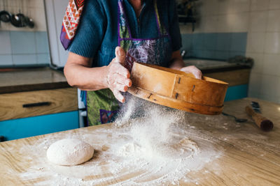 Midsection of woman sifting flour on table at home