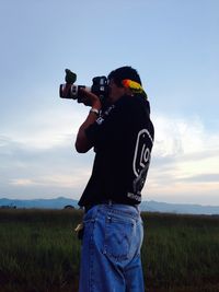 Man photographing camera on field against sky