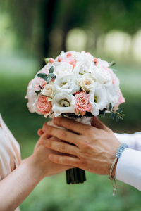 Close-up of bride and groom holding bunch of flowers outdoors