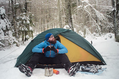 Young man camping in forest during winter