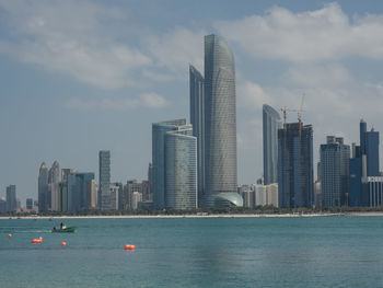 Sea by modern buildings against sky in city