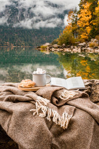 Picnic on stones in the bavarian mountains, germany. plaid, cacao, croissant, book near lake