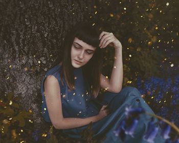 High angle view of leaves falling on thoughtful woman sitting by tree trunk