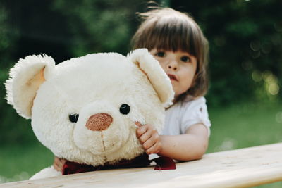 Portrait of girl holding teddy bear while standing by wooden railing