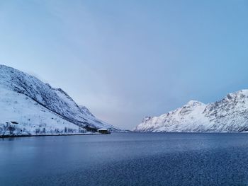 Scenic view of sea by snowcapped mountains against sky