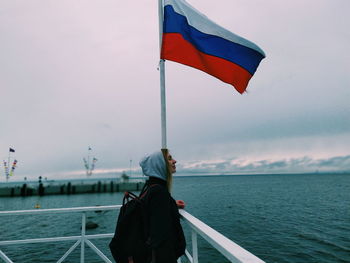 Woman standing at observation point by flag by sea against sky