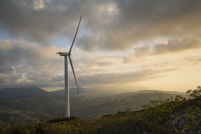 Wind turbines on landscape against sky during sunset