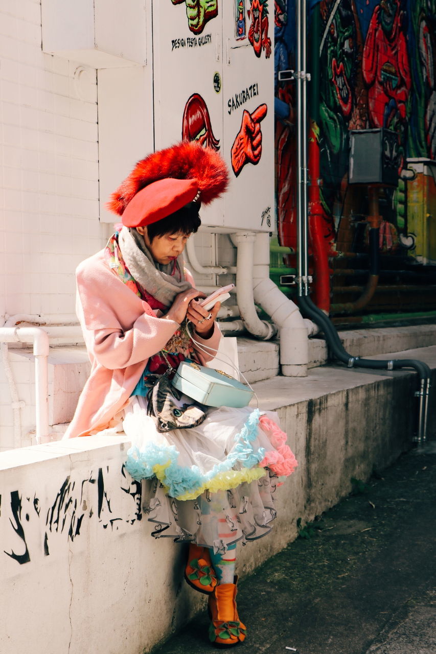 art, red, one person, full length, street, adult, architecture, clothing, road, person, lifestyles, women, day, creativity, standing, men, graffiti, city, outdoors, casual clothing, footwear, performance art, female, holding