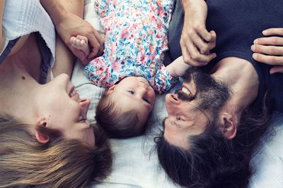 High angle view of baby girl lying amidst parents on bed at home