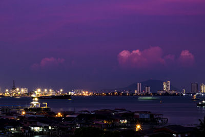 Illuminated cityscape by sea against sky at night