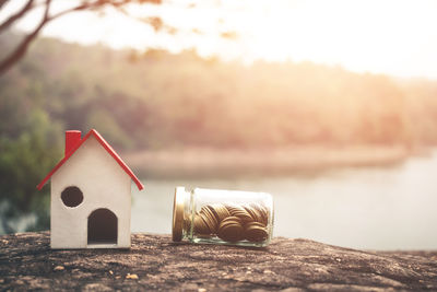 Coins in jar and model house against lake on rock