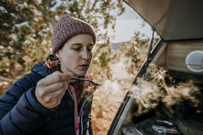 Woman blows hot steaming spoonful of soup while camping with camper