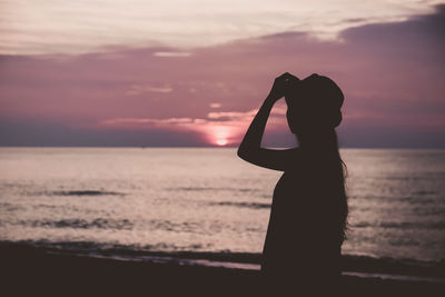 Silhouette woman standing at beach against sky during sunset