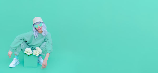 Full length portrait of woman holding flower crouching over colored background