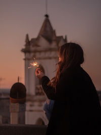 Women holding sparkler sitting against sky during sunset