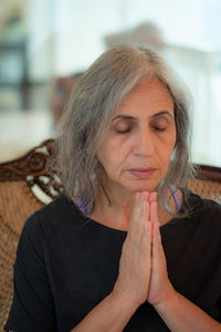 Senior woman with hands clasped sitting on sofa at home