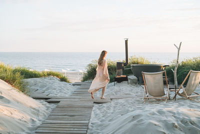 Rear view of woman sitting on beach against sky