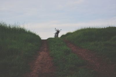 Dirt road amidst field against sky