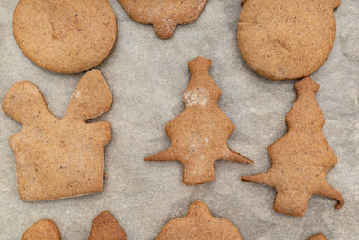 Baked gingerbread cookies in various shapes without decorations, lying on baking paper, top view.