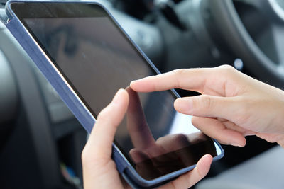 Cropped image of woman using digital tablet in car