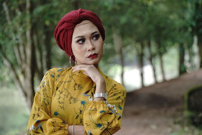 Woman looking away while wearing headscarf against trees