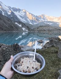 Midsection of person with ice cream on mountain against sky