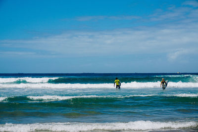 Rear view of friends with surfboards walking in sea against sky