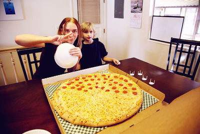 Portrait of happy siblings with pizza at table