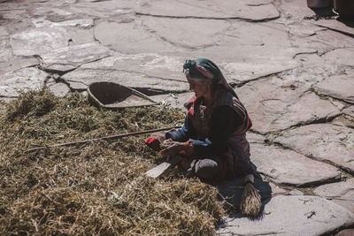 Side view of woman sitting by hays on footpath during sunny day