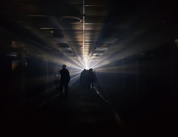 Rear view of silhouette people walking in illuminated tunnel