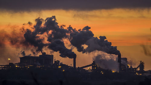 Smoke emitting from factory against sky during sunset