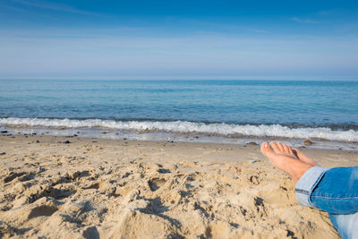 Low section of person at beach against sky