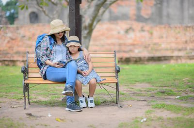 Full length of mother and daughter sitting on bench at park