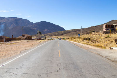 Road leading towards mountains against clear sky