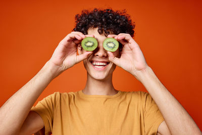 Man holding kiwi while standing against orange background