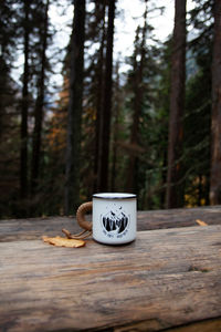 Coffee cup on table against trees in forest