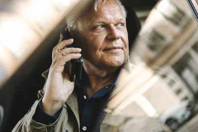 Contemplative senior businessman talking on smart phone while sitting in car