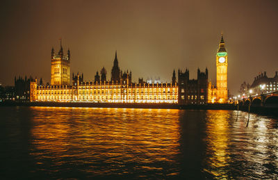 Illuminated buildings by river against sky in city at night