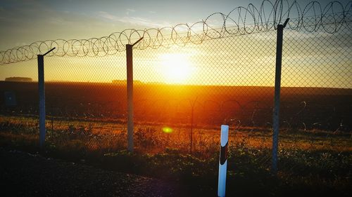 Fence on field against sky during sunset