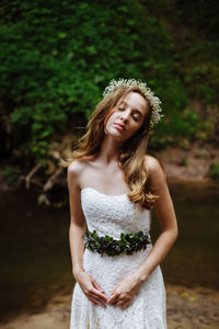 Beautiful young bride with eyes closed standing in forest