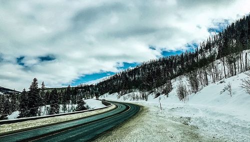 Snow covered road by trees against sky