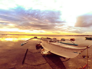 Boats moored on beach against sky during sunset